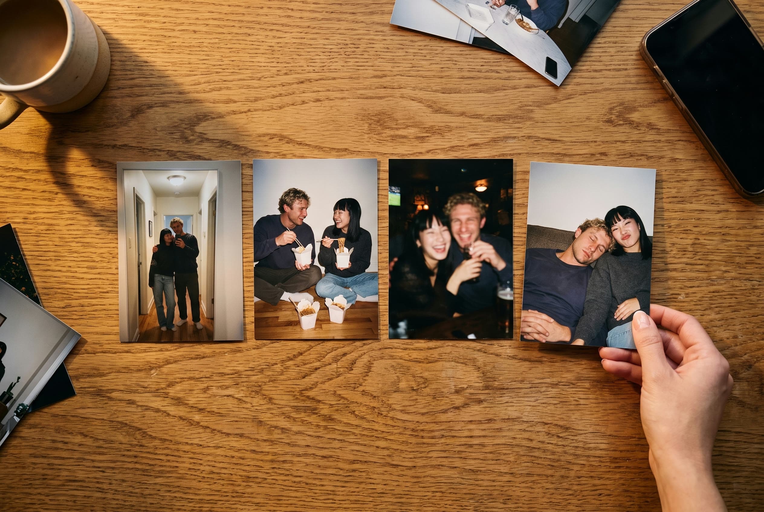 A hand placing the last of four printed photos of a couple in a row on a wooden table.