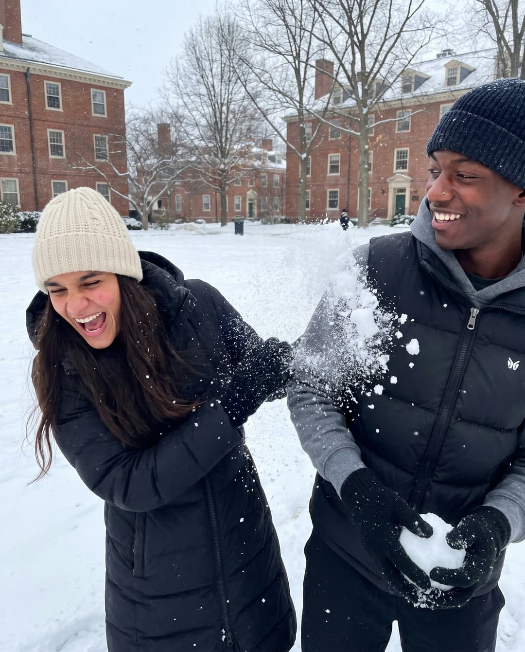 Ren and Kavi laughing mid-snowball-fight on a snowy campus lawn.